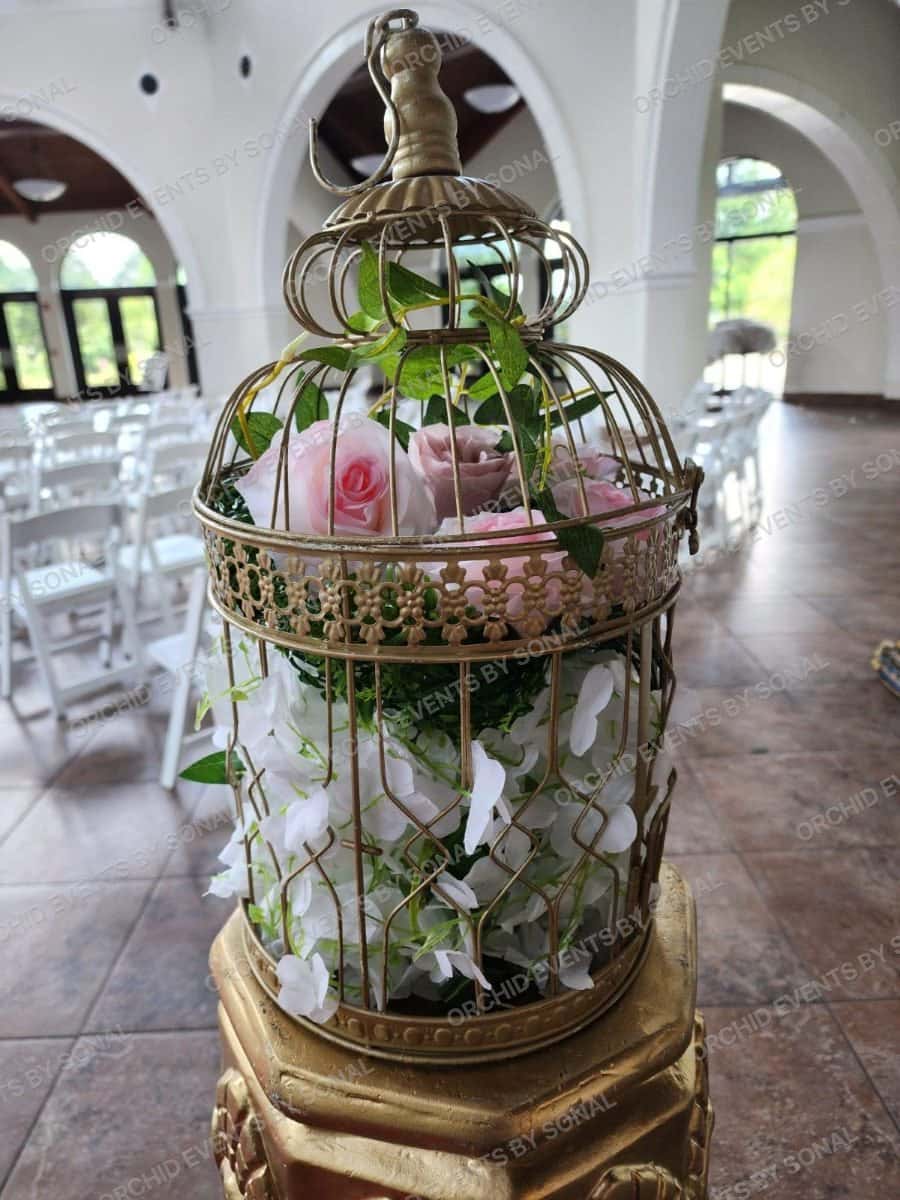 Gilded birdcage centrepiece filled with roses and foliage on a carved plinth