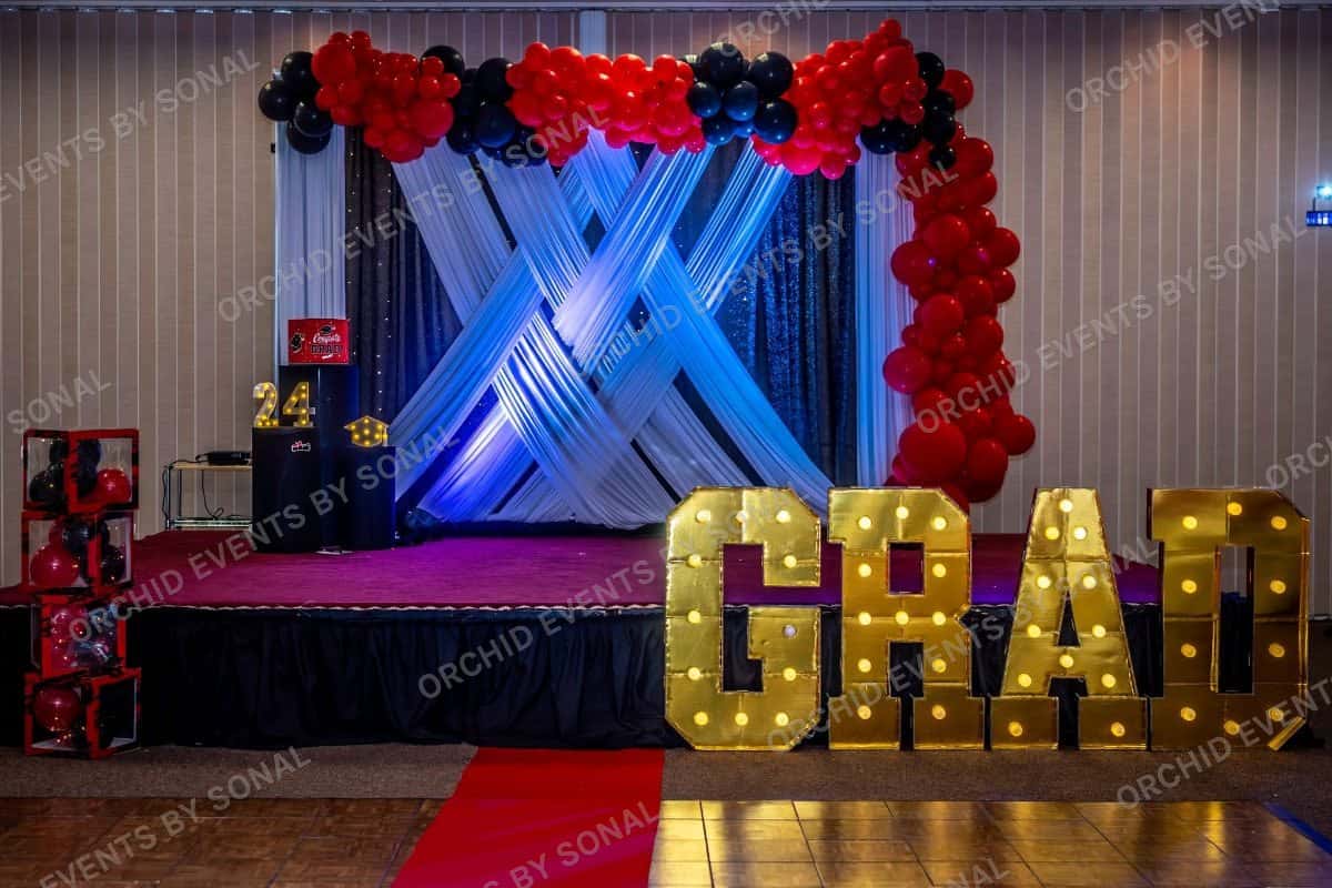 Graduation stage in navy and red with lit GRAD marquee letters on a red carpet