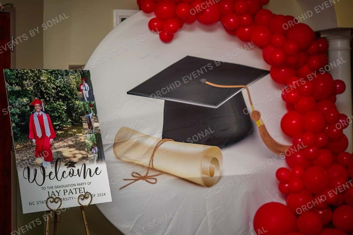 Graduation welcome easel beside a red balloon arch and a mortarboard cutout
