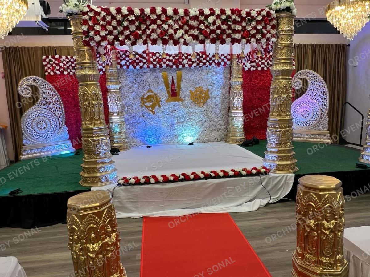 Gold-pillared mandap with red and white garlands and a red carpet approach