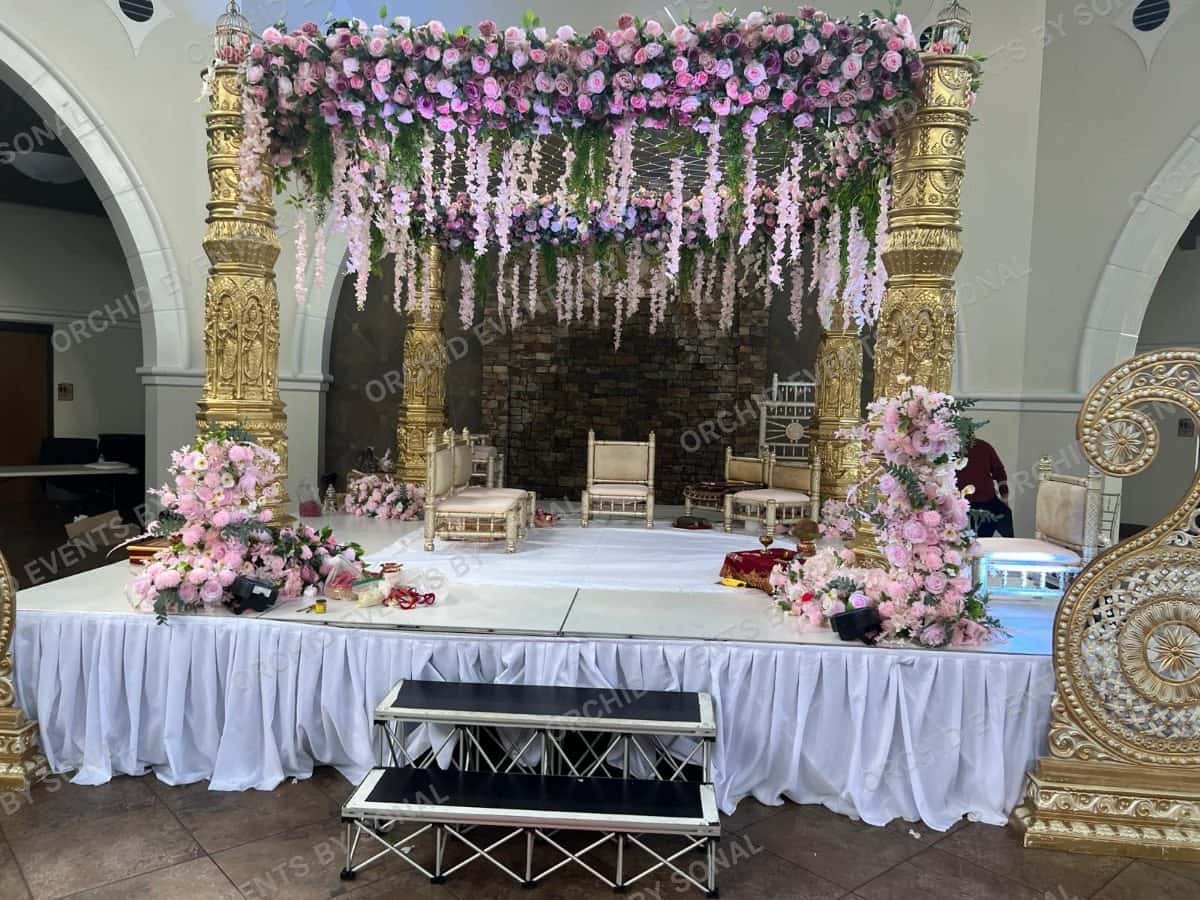 Gold mandap hung with pink wisteria and blossom over a white stage