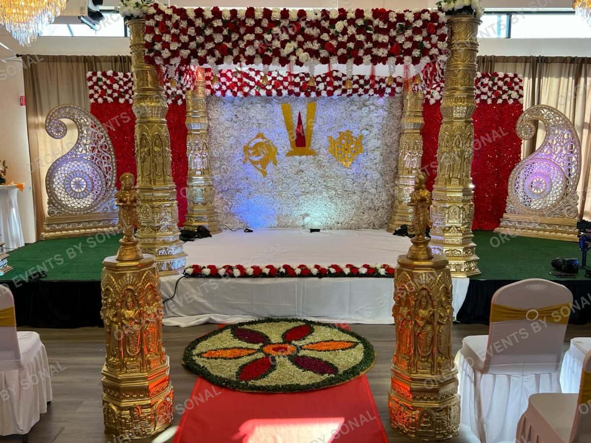 Carved gold mandap with red and white flower garlands over a raised stage