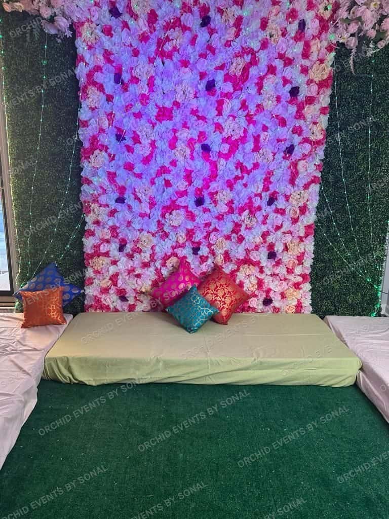 Pink and white flower wall behind a low mehndi seat with embroidered cushions