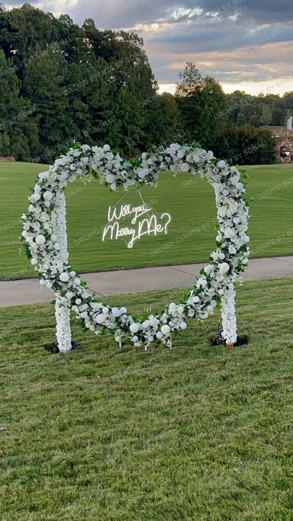 White floral heart arch standing on a golf-course lawn for a proposal