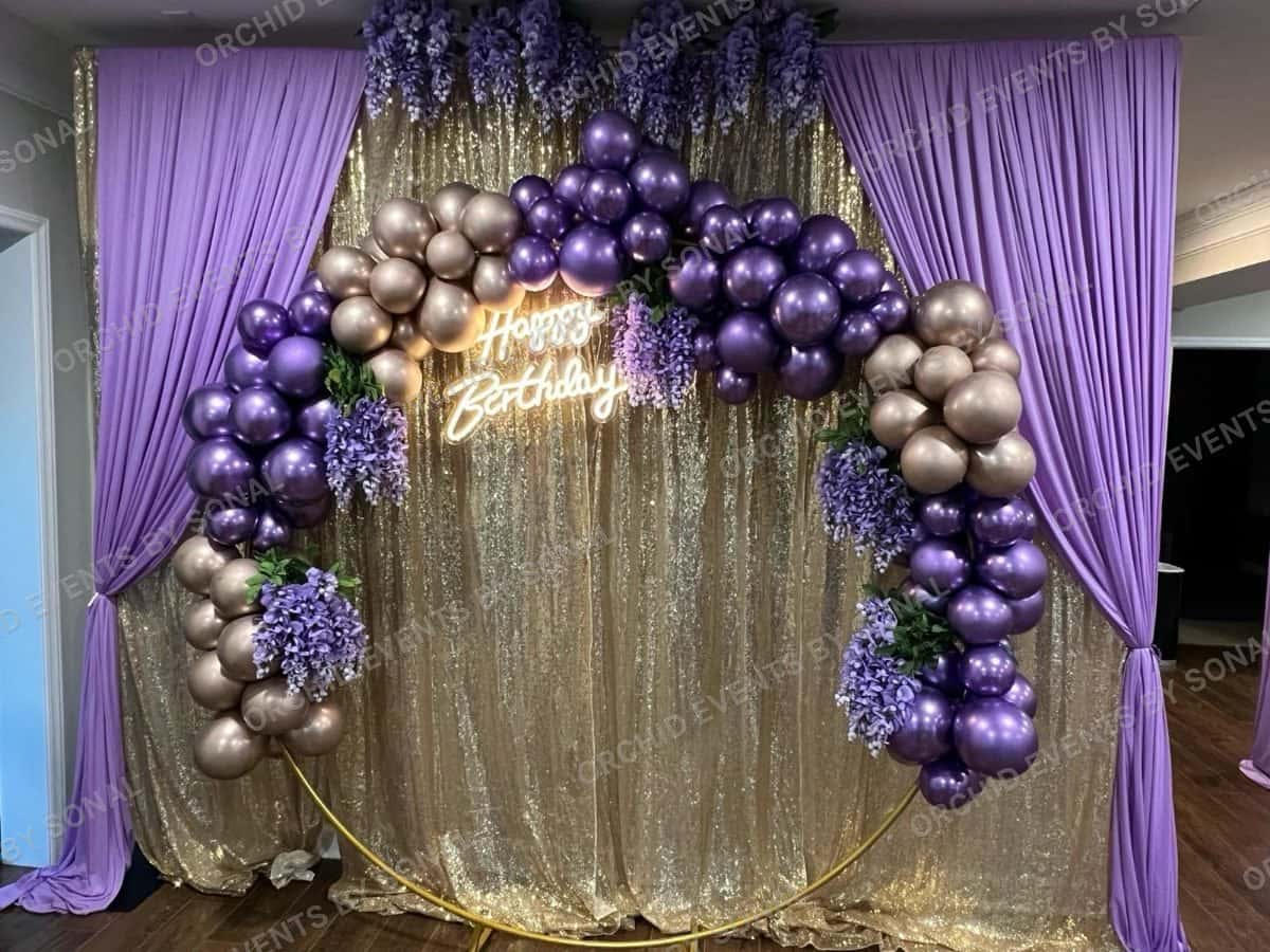 Purple and chrome balloon clusters on a gold sequin backdrop with a neon birthday sign