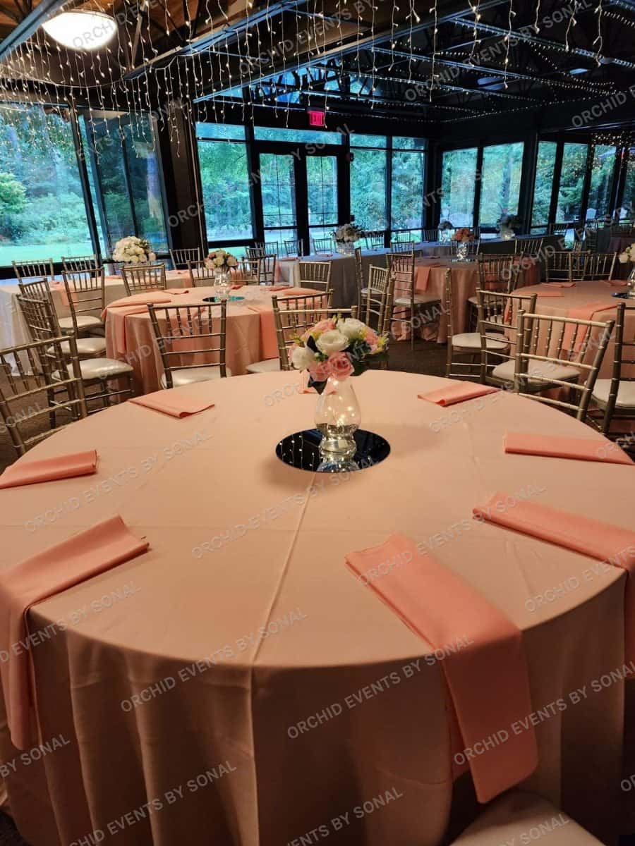 Round reception table in peach linen with gold chiavari chairs and a low centrepiece