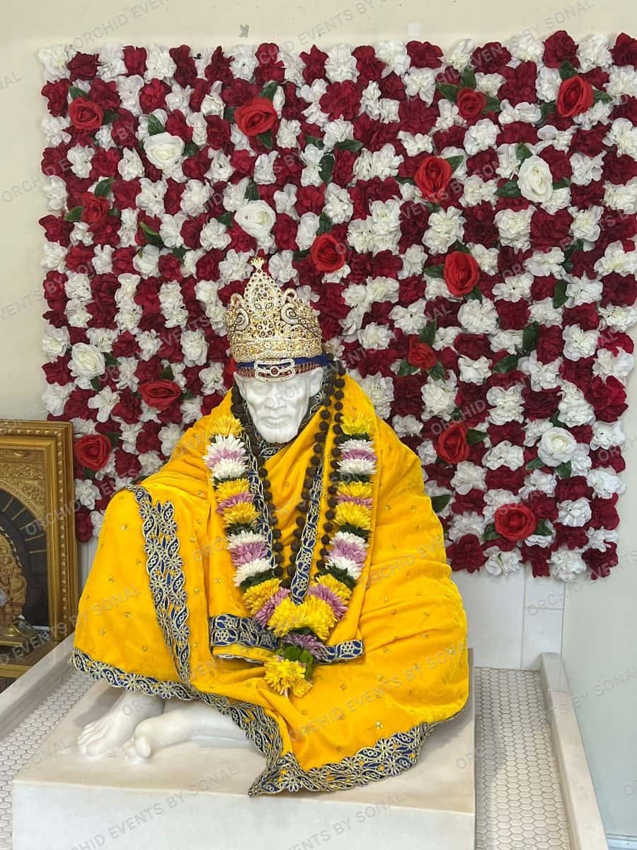 Sai Baba shrine dressed in gold and garlands against a red and white rose wall