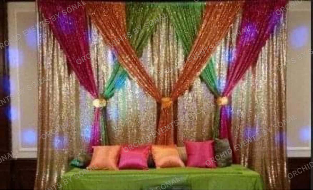Sangeet stage in gold sequin and jewel-toned drapes with a low cushioned seat