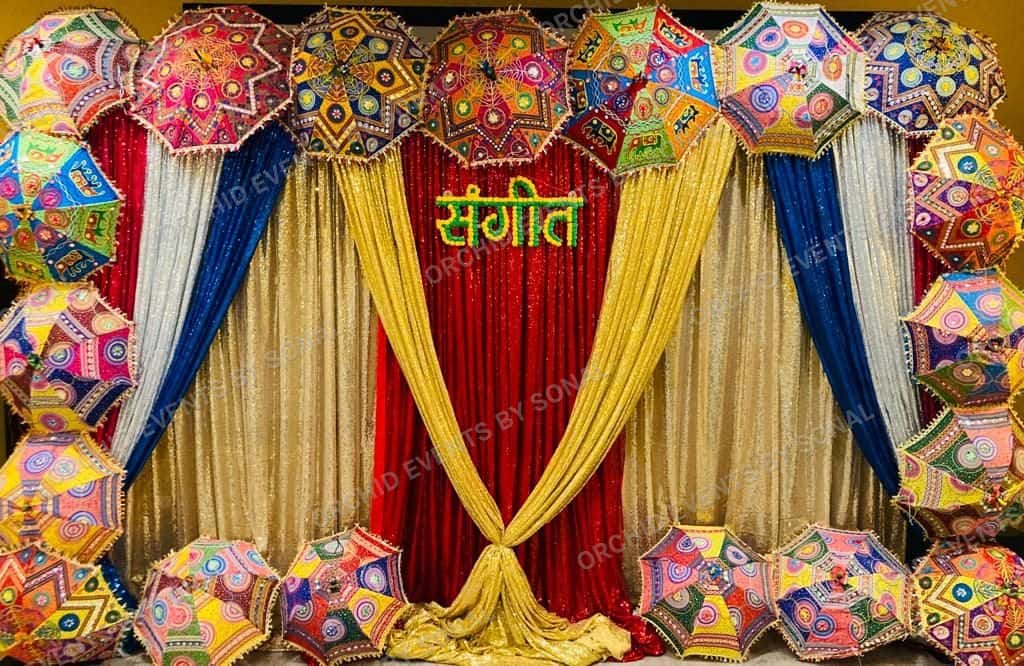 Sangeet backdrop in red, gold and navy drape crowned with mirrored umbrellas